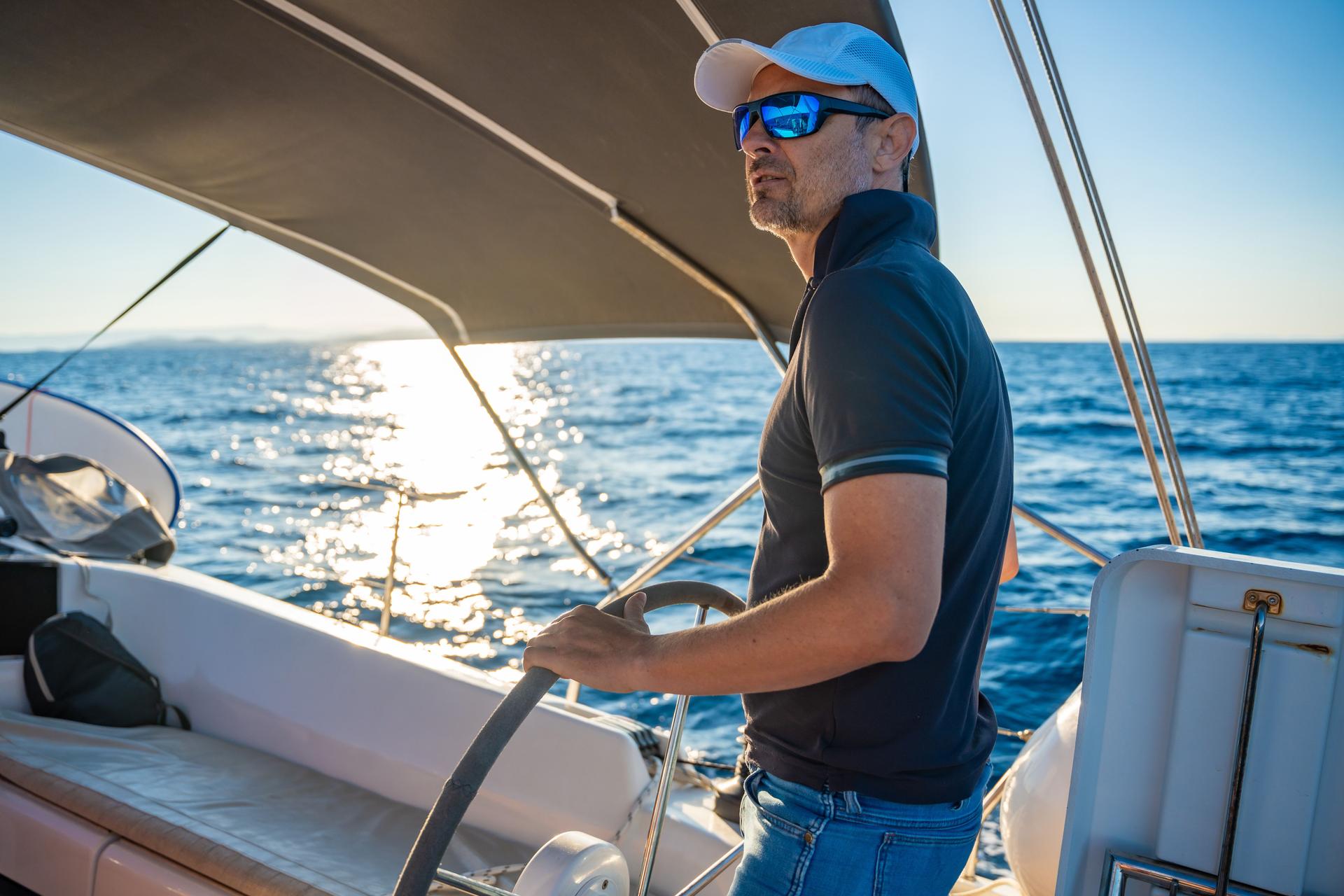 Young man captain stands at the helm and controls a sailboat during a journey by sea